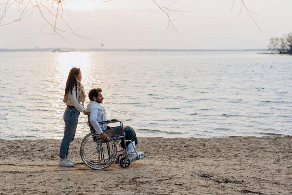 Image of man in a wheelchair with woman pushing him on a beach